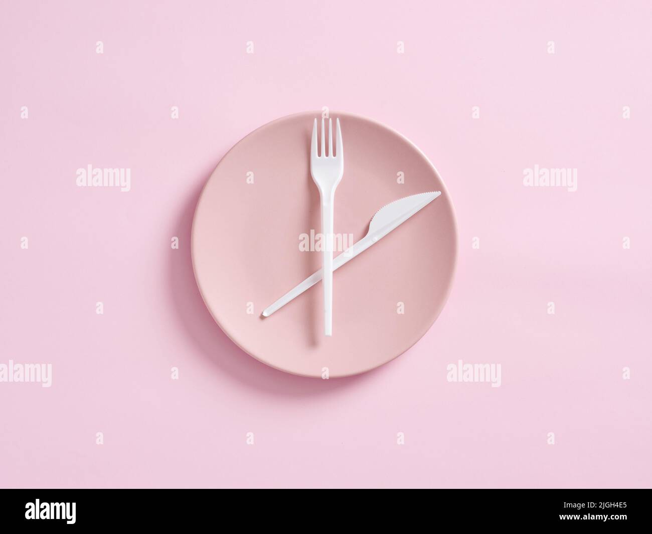 Messer und Gabel auf rosafarbenem Teller als Uhr. Intermittierendes Fasten, Mittagessen, Gewichtsverlust, Mahlzeit Plan oder Diät-Konzept. Stockfoto