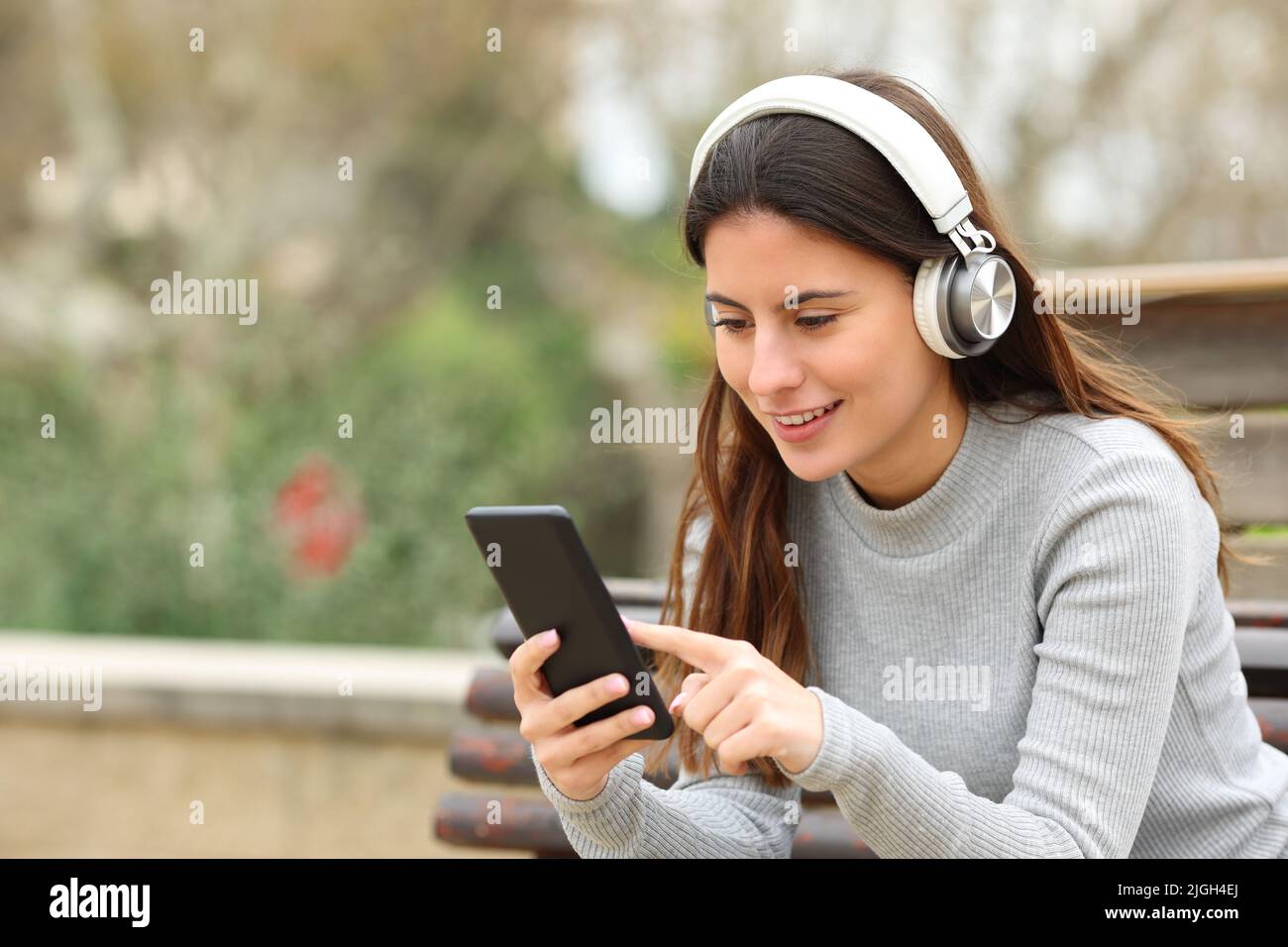 Fröhlicher Teenager, der in einem Park Smartphone mit Kopfhörern Musik hört Stockfoto