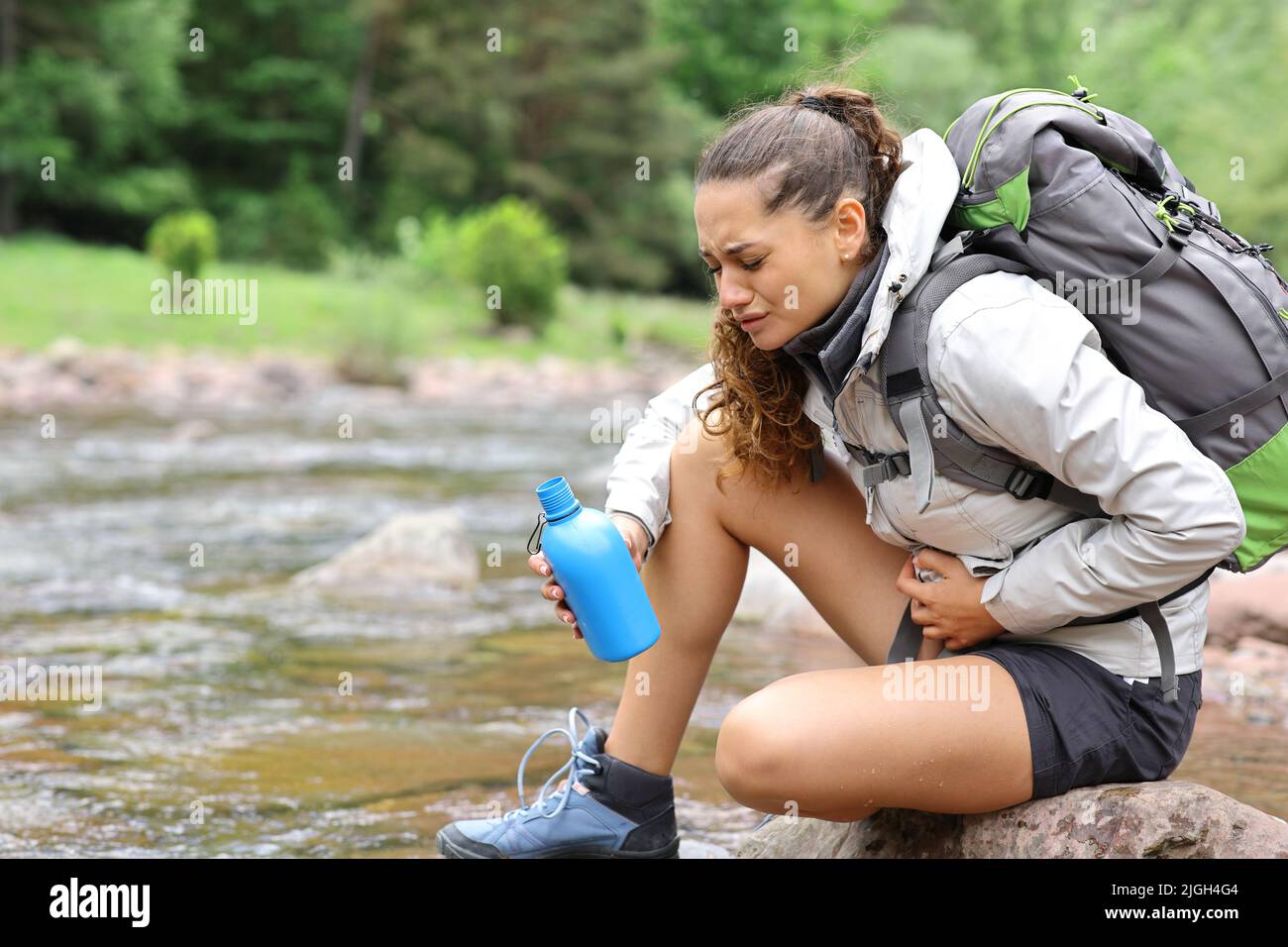 Gestresste Wanderer allein leiden Bauchschmerzen nach dem Trinken von Flusswasser in den Bergen Stockfoto