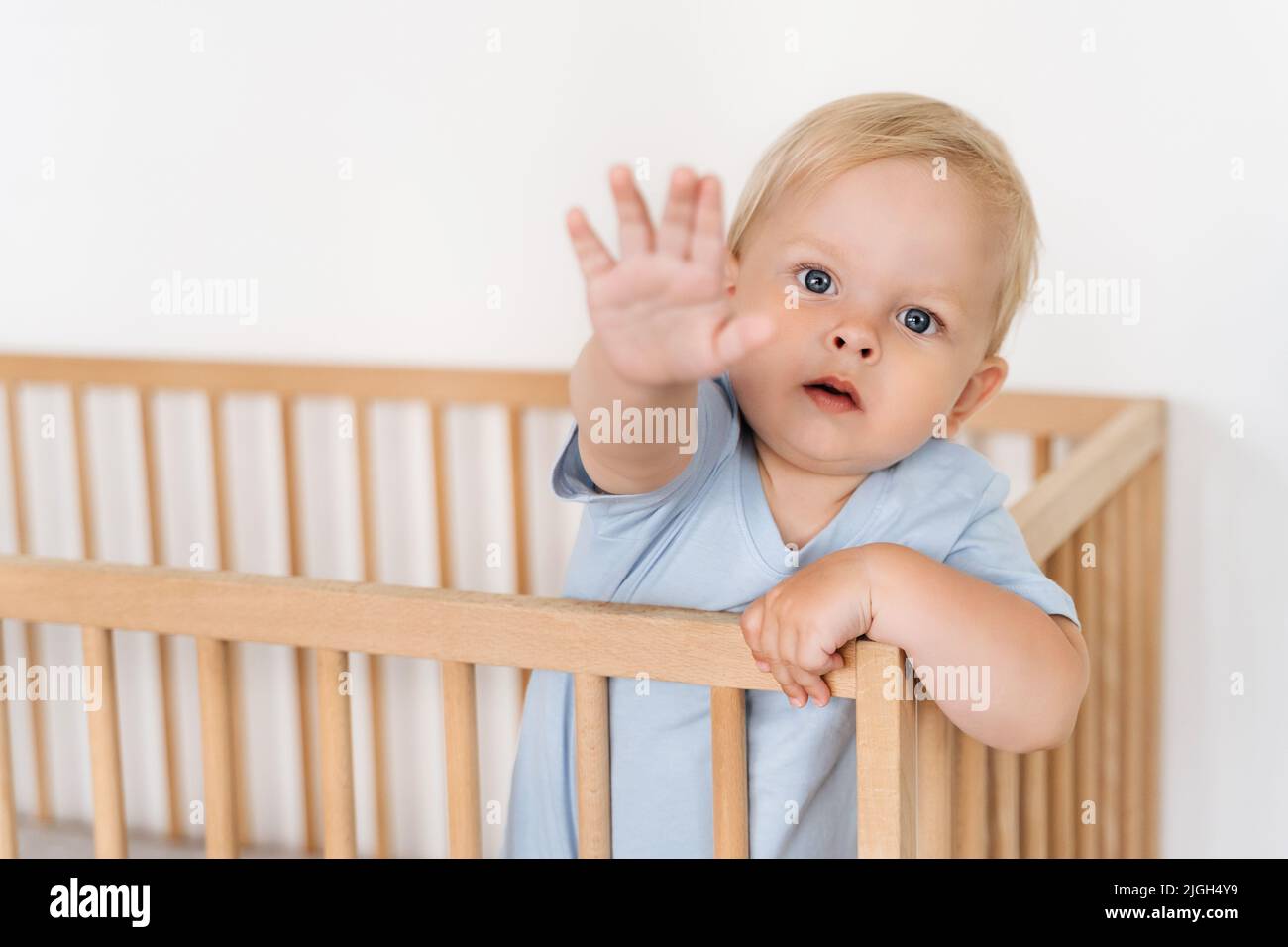 Indoor-Porträt der besorgt aufgeregt kaukasischen Baby in Holzbett auf weißem Hintergrund zu erreichen Hand aus bitten, ihn abzuholen. Kinderbetreuung, Kindheit, Mutterschaftskonzept Stockfoto