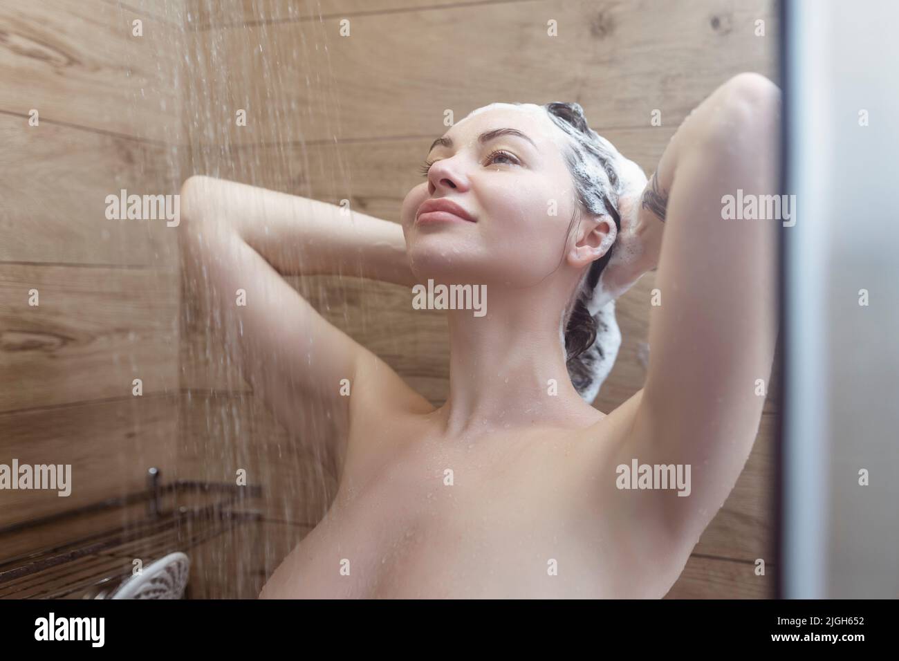 Schöne nackte junge Frau wäscht ihr Haar und verwendet Shampoo, während eine Dusche im Badezimmer Stockfoto