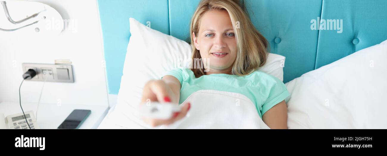 Glückliche Frau, die im Bett lag und mit der Fernbedienung den Sender im fernseher gewechselt hat Stockfoto