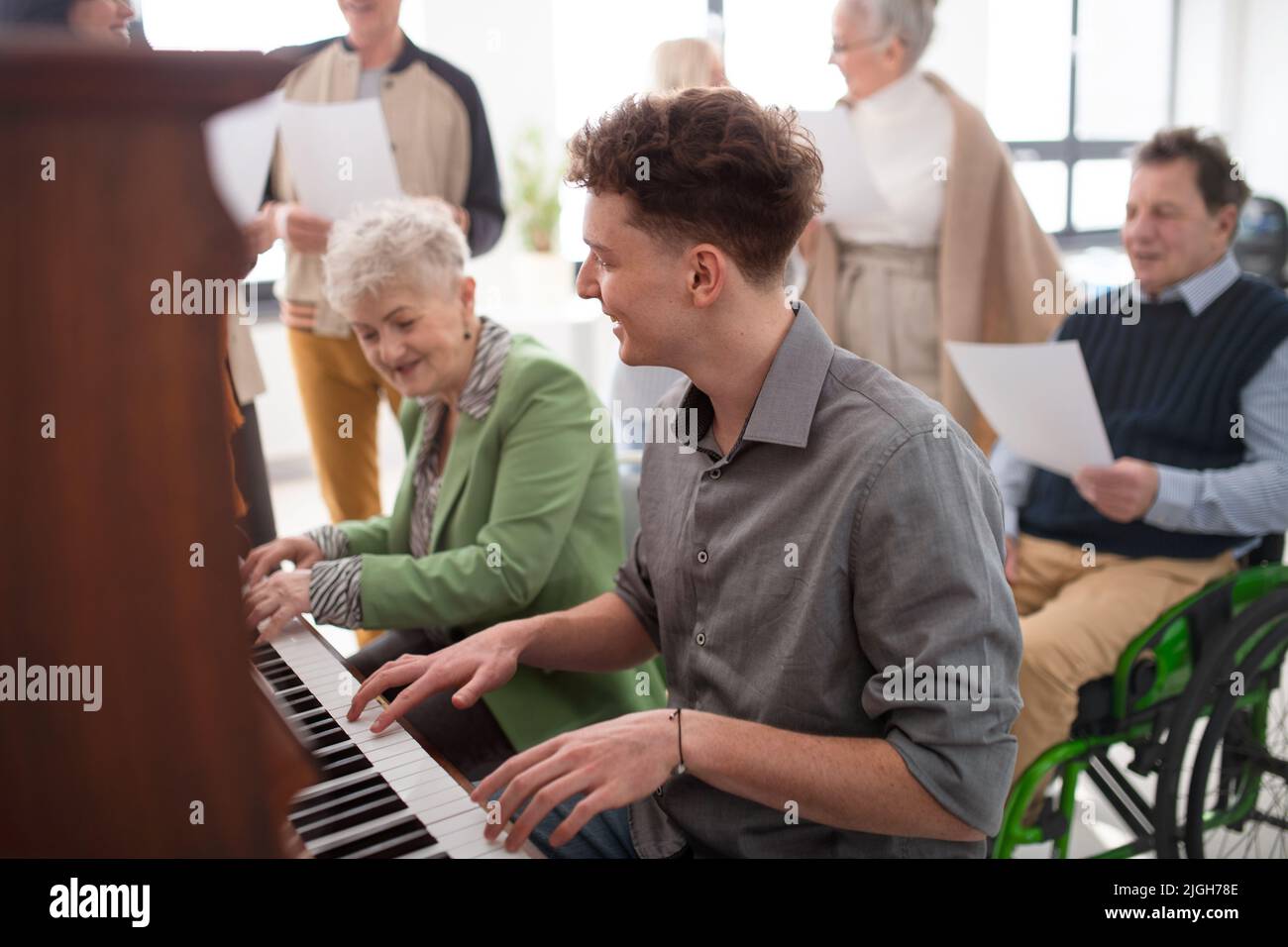 Ältere Frau mit junger Lehrerin, die bei der Chorprobe am Klavier spielt. Stockfoto