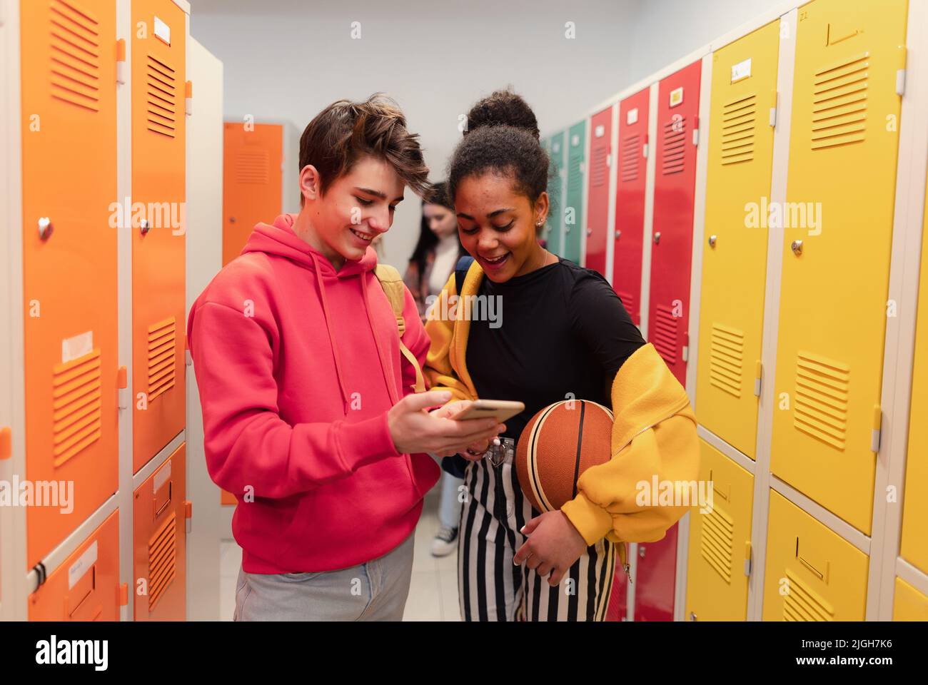 Junge Gymnasiasten, die in der Nähe von Schließfächern im Flur auf dem Campus stehen und mit dem Smartphone sprechen. Stockfoto