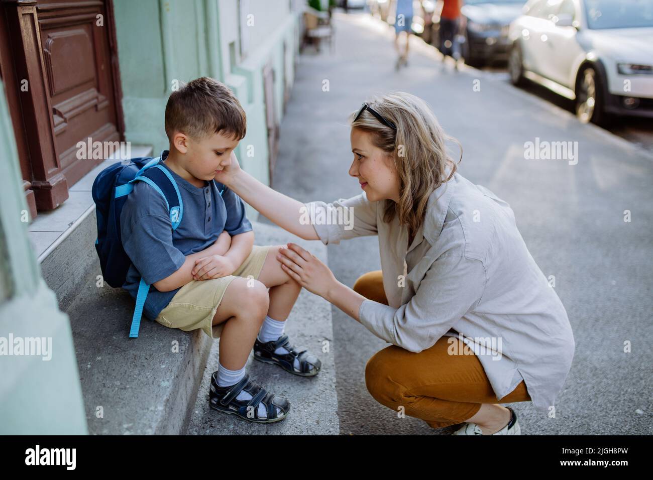 Mutter tröstete ihren kleinen Sohn an seinem ersten Schultag, saß auf einer Treppe und sagte vor der Schule Auf Wiedersehen. Stockfoto