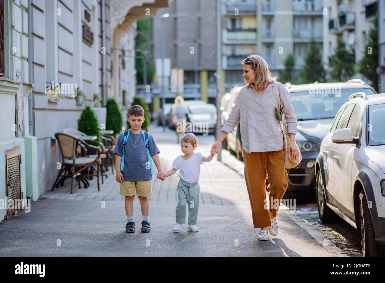 Junge Mutter mit Null-Abfall-Einkaufstasche, die Hände mit ihren Kindern hält und in der Stadtstraße läuft Stockfoto