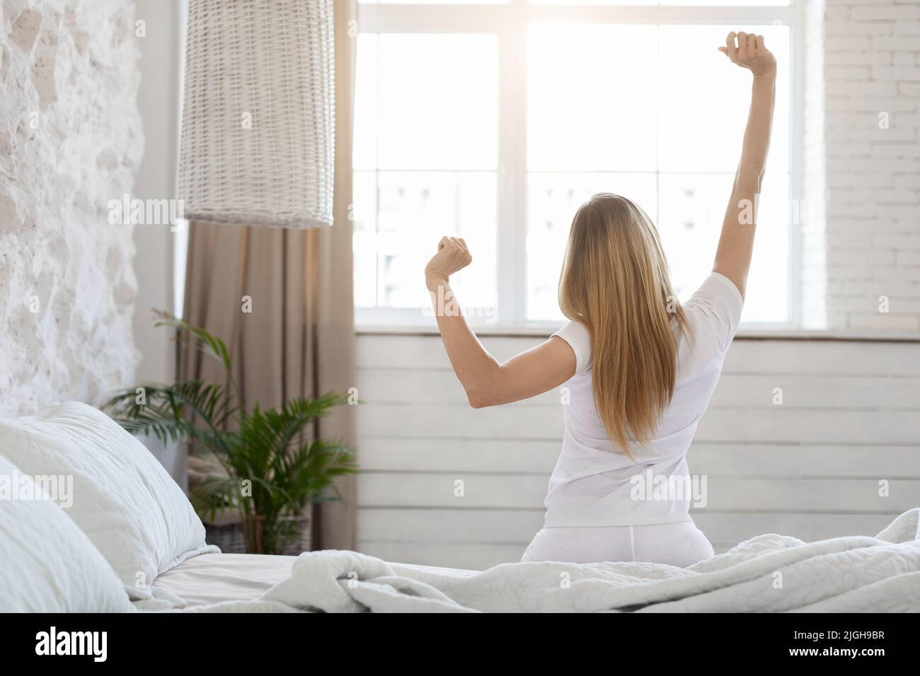 Unverkennbare blonde Frau genießt fröhlichen Morgen, Stretching im Bett Stockfoto