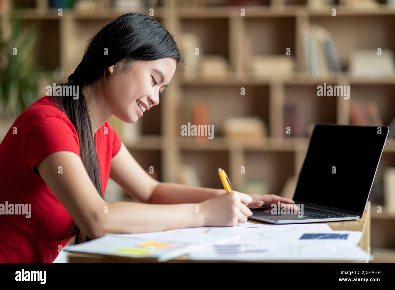 Fröhliche Jugendliche japanische Dame machen Hausaufgaben, bereiten Sie sich auf die Prüfung mit Laptop mit leerem Bildschirm studieren Stockfoto
