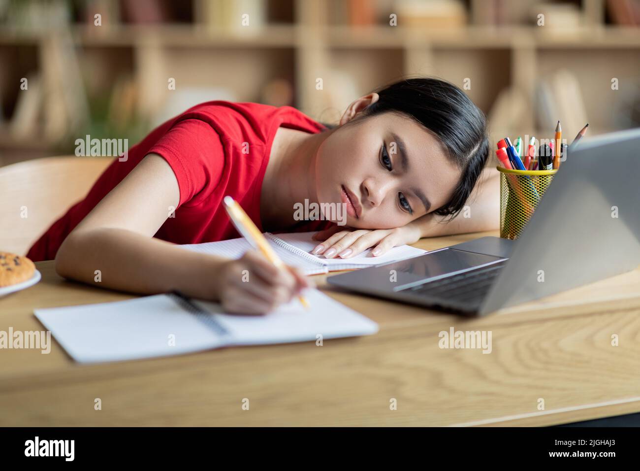 Müde Jugendliche japanische Studentin liegt auf dem Tisch in der Nähe des Computers im Innenraum des Zimmers Stockfoto