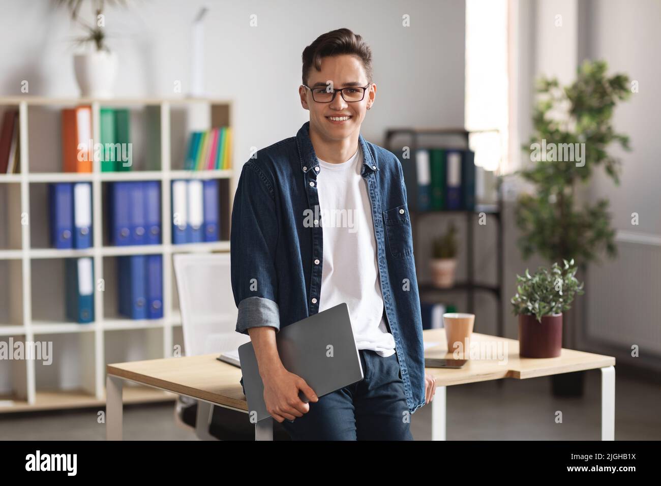 Modernes Unternehmertum. Millennial Businessman Holding Laptop Steht In Der Nähe Des Schreibtisches Im Büro Stockfoto