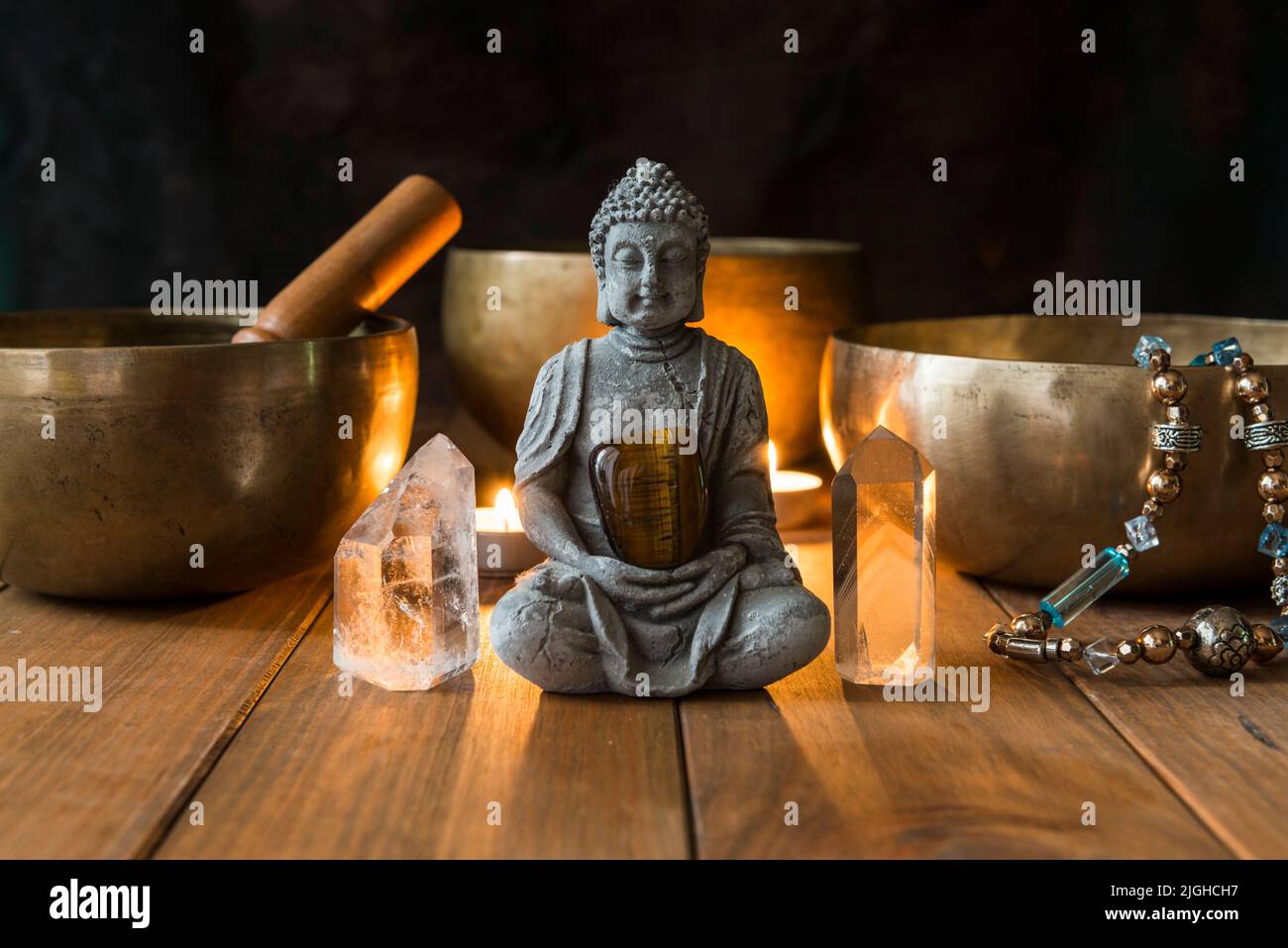 Stillleben mit Klangschalen, Mineralien, Kerzen und einer Buddha-Figur auf Holzbrettern und einem dunklen Hintergrund. Kleiner Altar mit kleiner Kerze beleuchtet Stockfoto