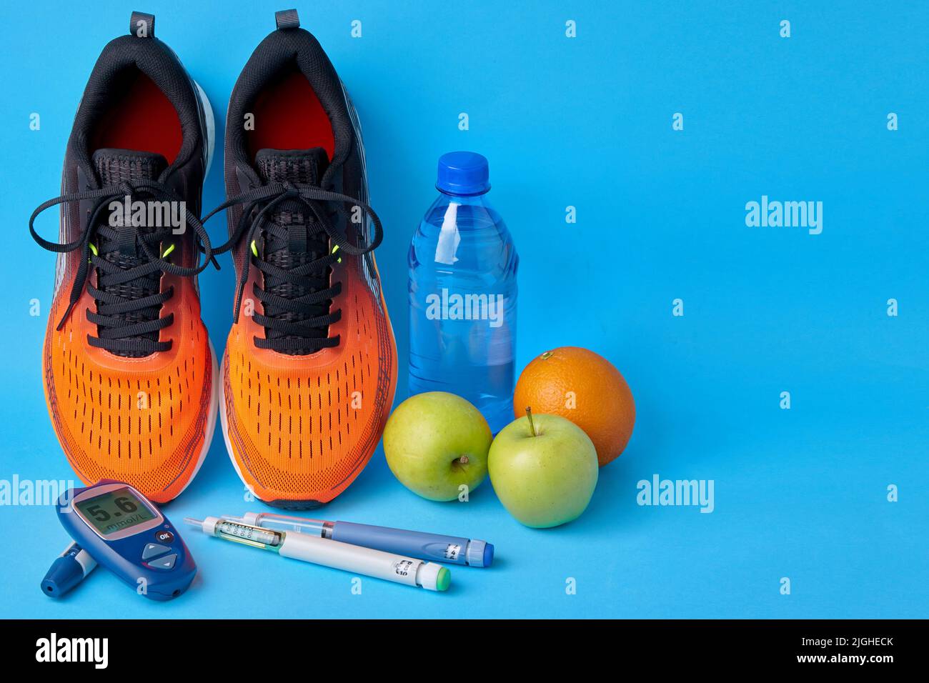Orangefarbene Sneakers, Früchte, Glucometer, Insulin-Spritzenstifte und Trinkwasserkasche aus Kunststoff auf blauem Hintergrund. Bewegung, Ernährung und Diabetes Mensch Stockfoto