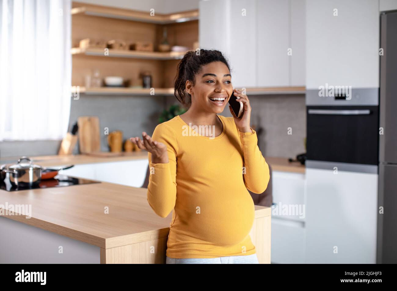 Fröhliche Millennial schwanger schwarze Frau mit großem Bauch spricht per Telefon, bekam gute Nachrichten und Klatsch Stockfoto