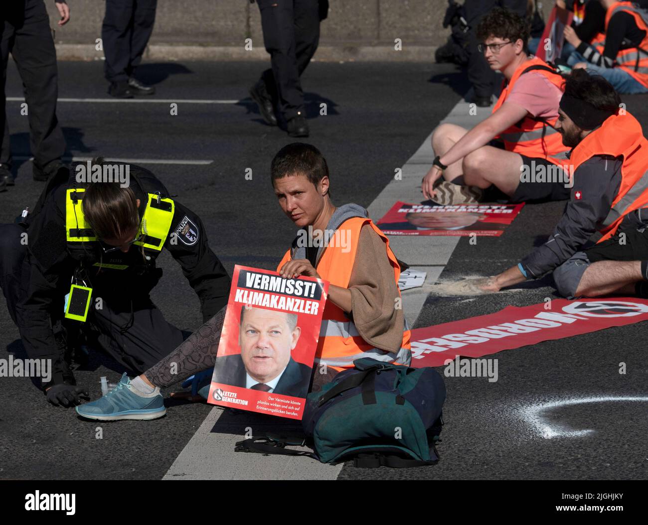 Berlin, Deutschland. 11.. Juli 2022. Klimaaktivisten der Gruppe "Last Generation" sitzen auf der Straße des ehemaligen ICC Berlin und blockieren den Verkehr - eine Frau hält ein Plakat mit Bundeskanzlerin Scholz und der Aufschrift "Missing - Climate Chancellor". An zahlreichen Orten in der Stadt haben die Aktivisten erneut Straßen blockiert. Quelle: Paul Zinken/dpa/Alamy Live News Stockfoto