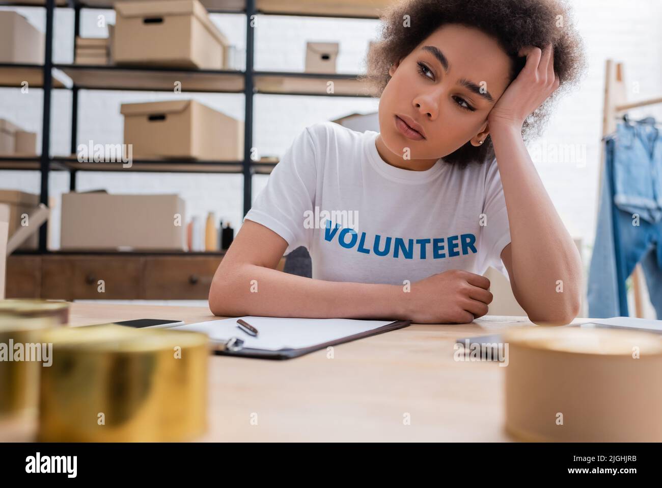 Müde und nachdenkliche afroamerikanische Freiwillige sitzen am Arbeitsplatz im Charity Center Stockfoto