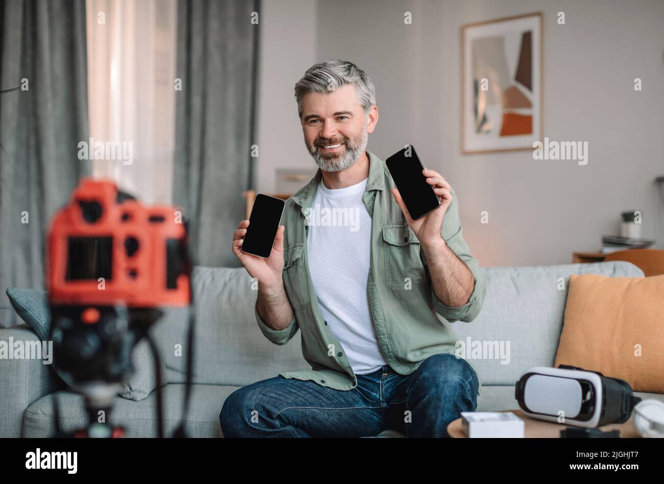 Glücklicher kaukasischer alter Mann mit Bart zeigt Smartphones mit leeren Bildschirmen und macht Videobesprechung im Wohnzimmer Stockfoto