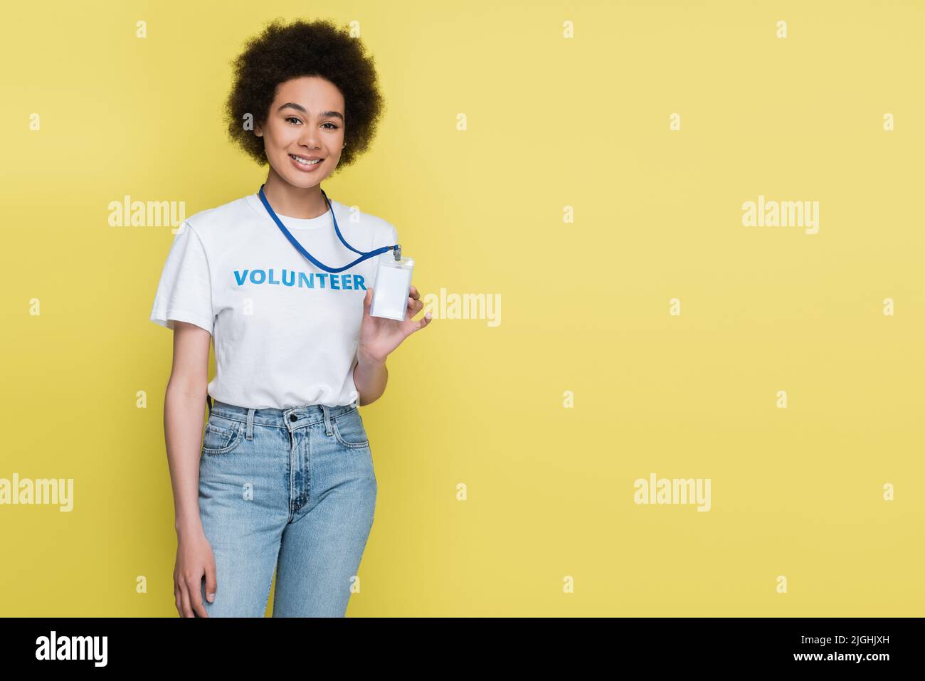 afroamerikanischer Freiwilliger lächelt der Kamera zu und zeigt einen leeren, auf Gelb isolierten ausweis Stockfoto