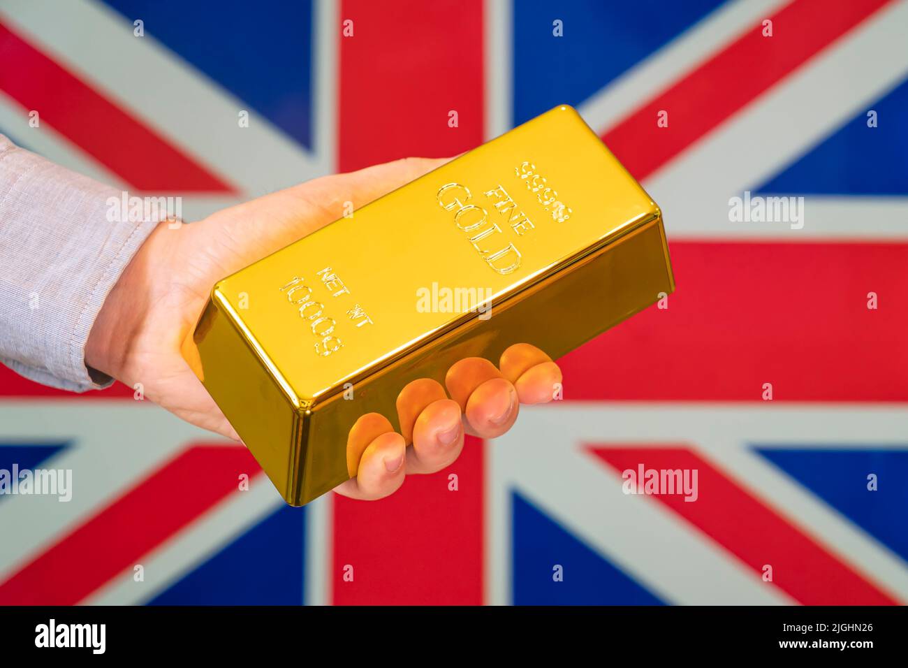 Die Goldreserve des britischen Konzepts. Goldbarren in der Hand auf dem Hintergrund der britischen Flagge Stockfoto