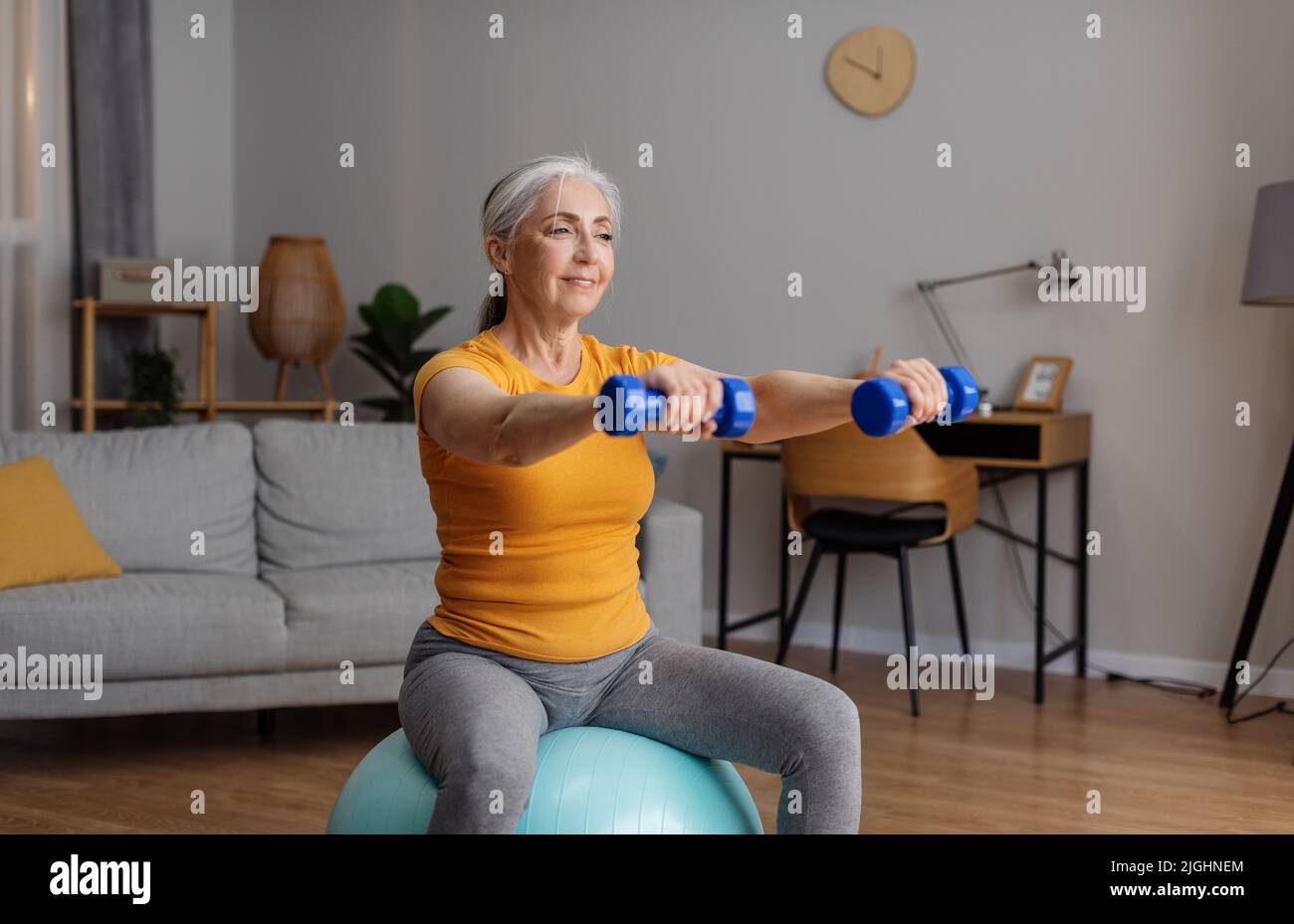 Aktive Pensionierung. Glückliche ältere Frau in Sportbekleidung trainieren mit Hanteln auf Fitball, mit inländischen Training Stockfoto