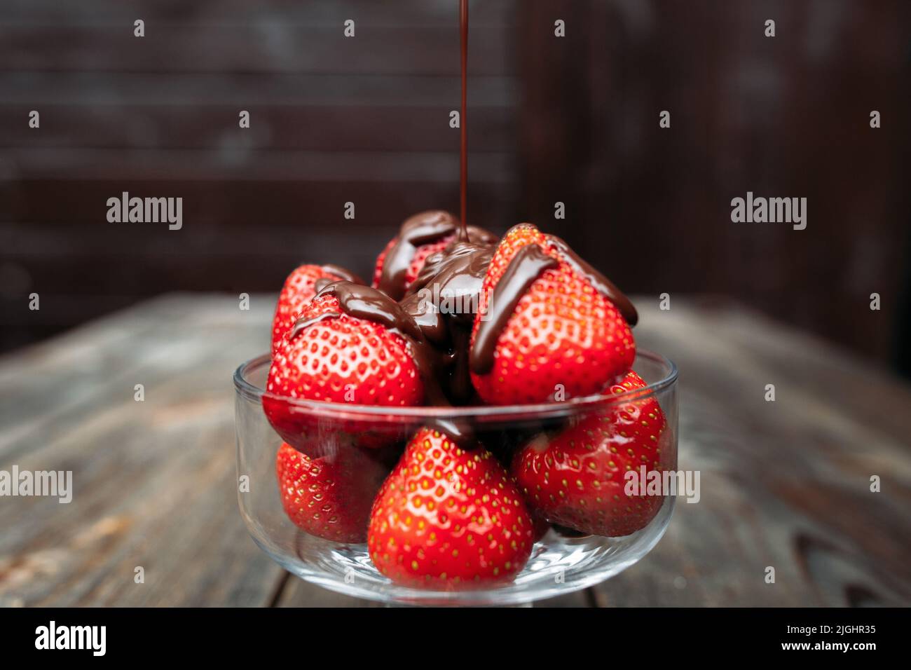 Gießen von Schokolade über Erdbeere, dunkler Hintergrund Stockfoto