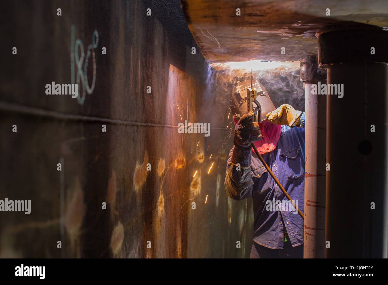 Schweißen männliche Arbeiter Metallbogen ist Teil der Maschinentank Düse Rohrleitung Bau Erdöl und Gas Lagertank in engen Räumen. Stockfoto