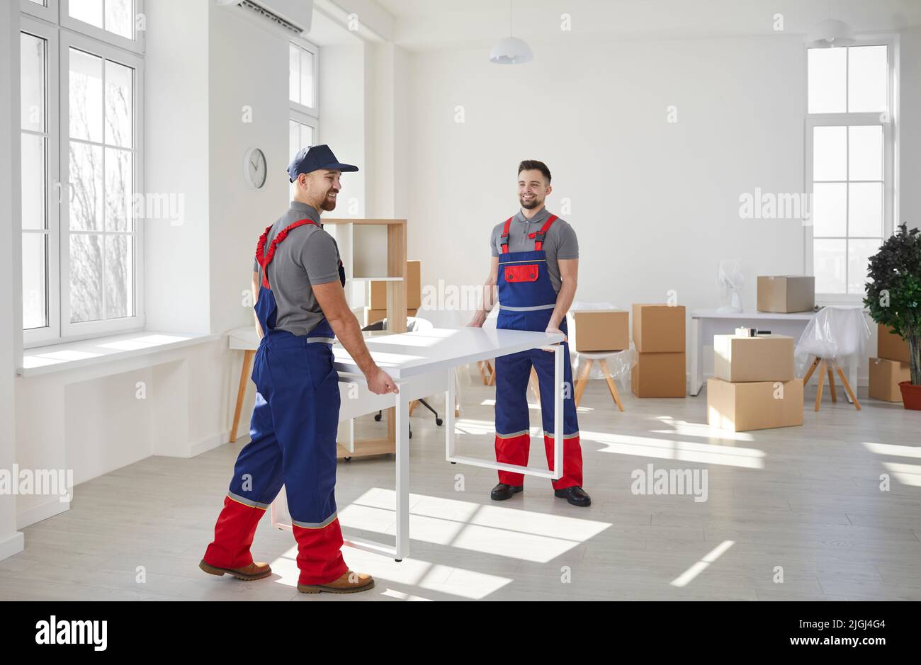 Zwei männliche umzugsdienstliche Mitarbeiter bewegen Möbel, wenn sie in ein Büro oder eine Wohnung ziehen. Stockfoto