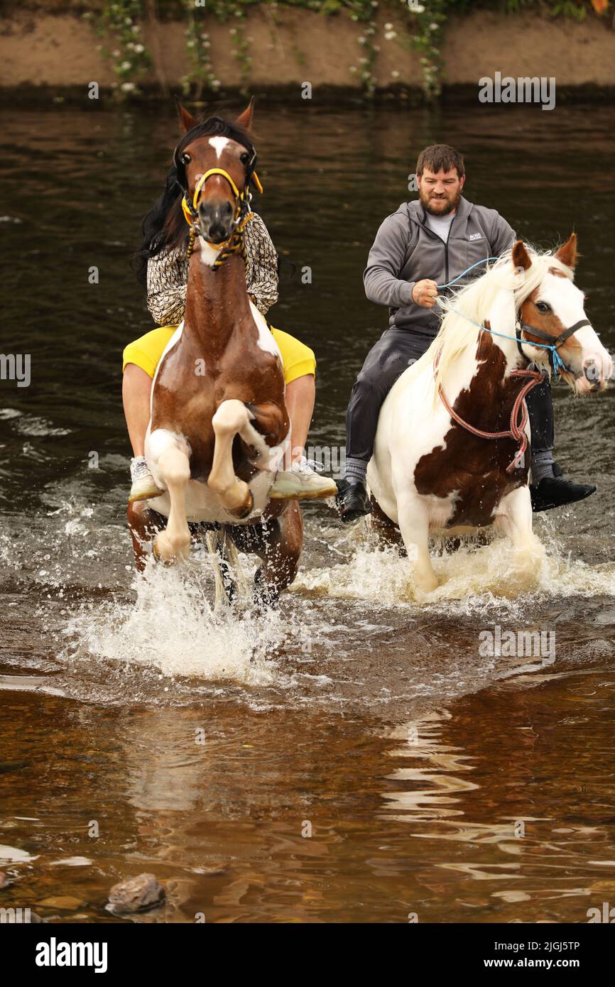 Ein junger Mann und eine junge Frau reiten auf ihren Pferden durch den Fluss Eden, Appleby Horse Fair, Appleby in Westmorland, Cumbria Stockfoto