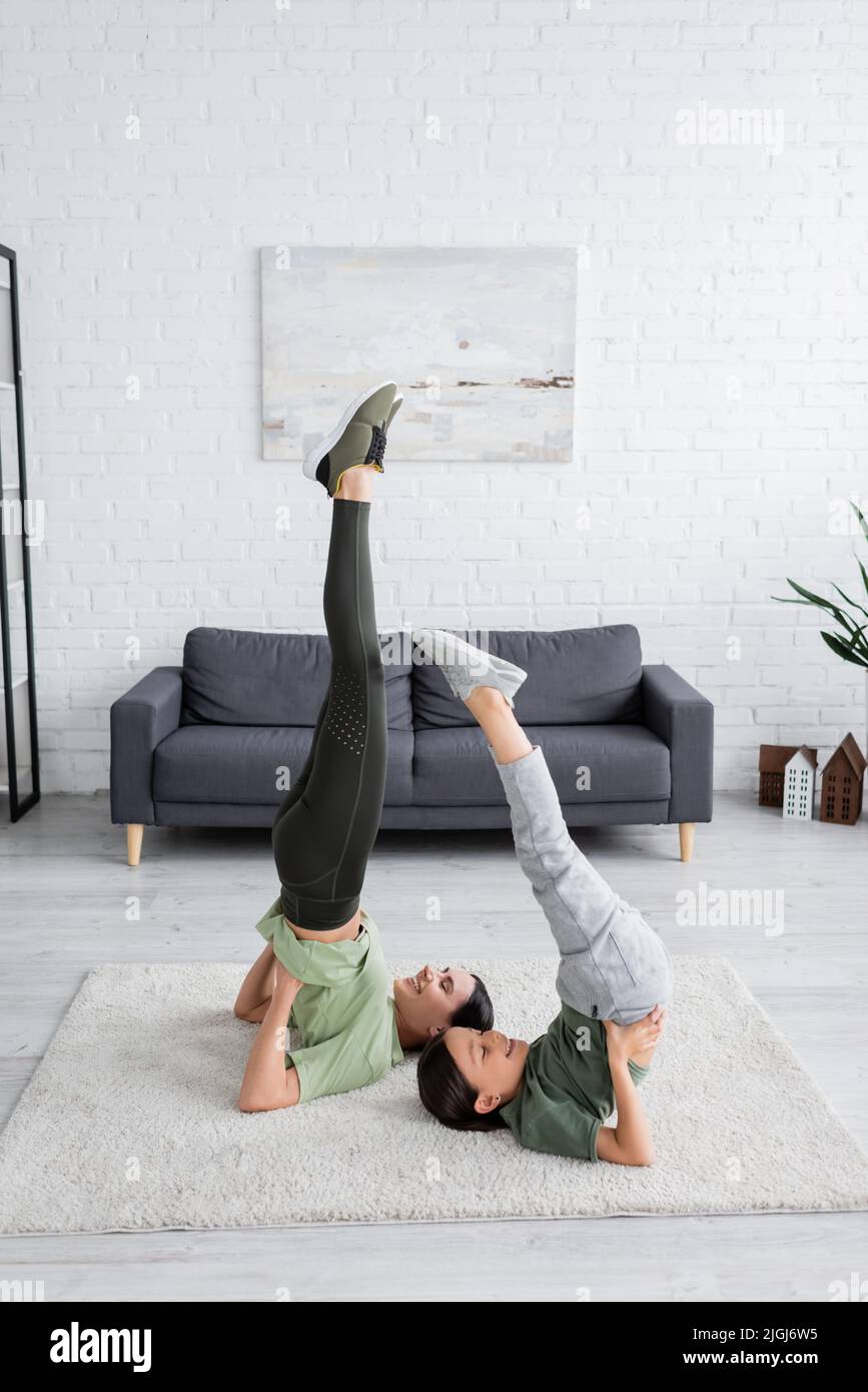 Happy girl mit Babysitter Training in unterstützten Schulterstand Pose auf Teppich im Wohnzimmer Stockfoto