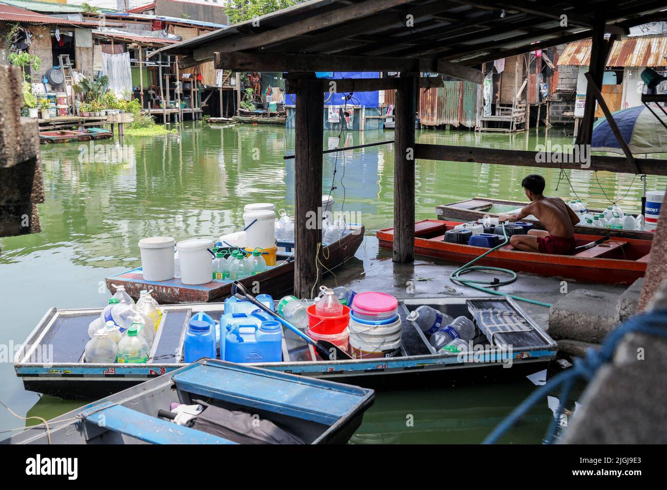 An einem kleinen Dock im Artex-Gelände in Malabon, Metro Manila, sammelt ein Mann Wasser aus Plastikbehältern. Das Dorf wurde seit mehreren Jahren von stagnierenden Gewässern überflutet. Die meist armen Bewohner müssen Boote für ihre täglichen Transportmittel benutzen, und selbst der Besuch ihrer Nachbarn ist zu einer mühsamen Anstrengung geworden. Um Zugang zu grundlegenden Notwendigkeiten wie Lebensmitteln zu erhalten, benötigen die Bewohner einen Transport zu anderen Teilen der Stadt, die nicht überflutet sind. Eines der größten Probleme für die Bewohner der Gegend ist es, sauberes Wasser für den Alltag zu bekommen. Philippinen. Stockfoto