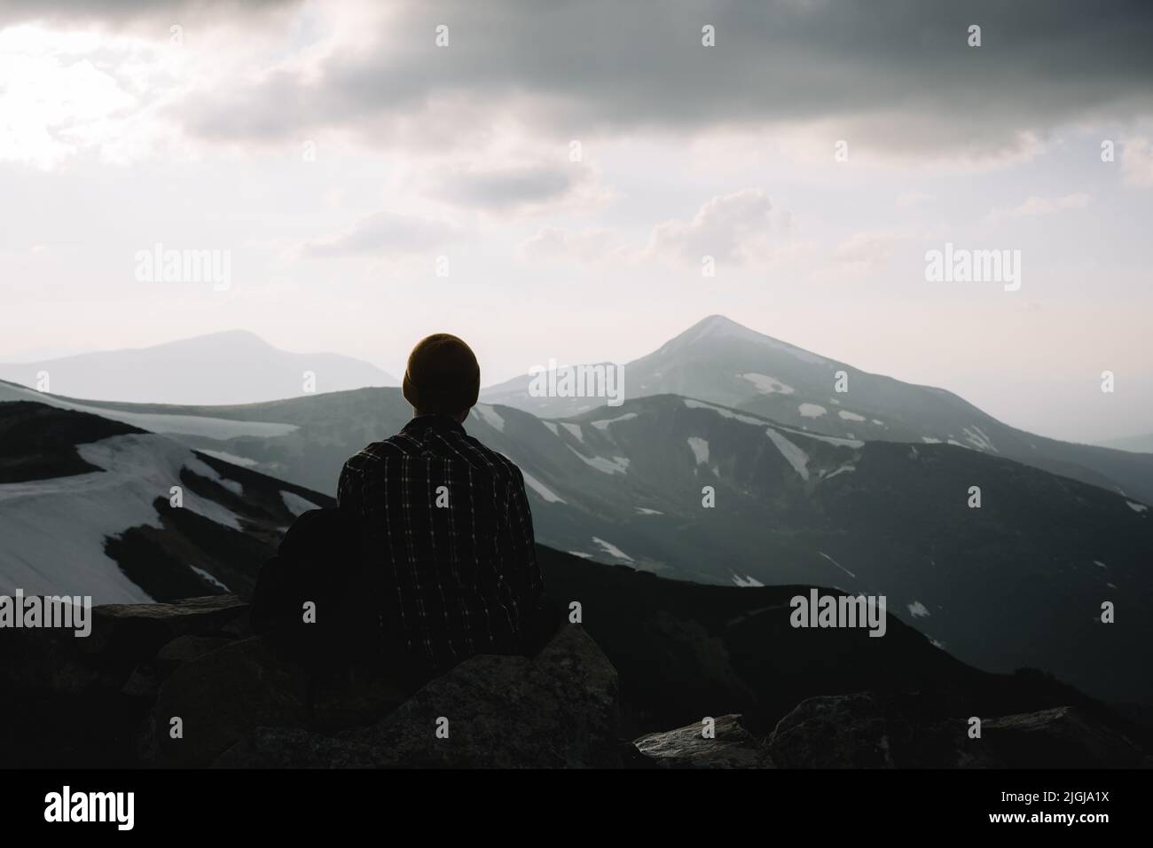 Ein Tourist sitzt am Rande eines Berggipfens. Neblige Berge im Hintergrund. Landschaftsfotografie Stockfoto