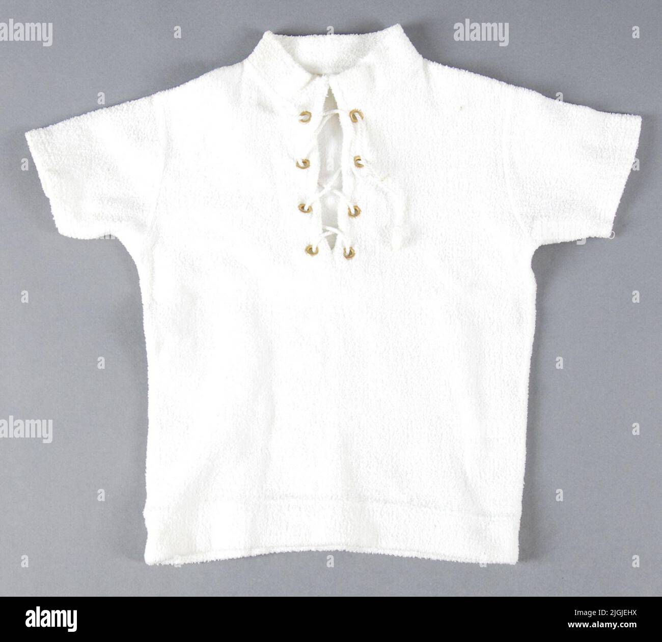 Tröja Kinderhemd aus weißer Baumwolle Frottee mit kurzen Ärmeln, Stehkragen und streuen. Die Streuung mit 8 gelben Metallringen ausgekleidet und wird mit weißem Twist zusammengehalten. Länge 390 mm, Brustbreite 320 mm, Ärmellänge 110 mm. Ausgewaschen, leicht vergilbt und gepunktet. Verwendet von Morgan Olsson, Swan Hall 2014 von Morgan Olsson, Svanhalla Stockfoto