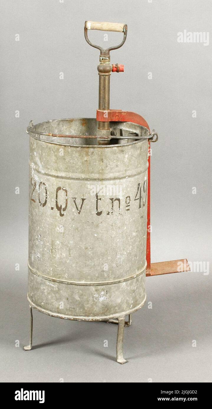 Brandspruta Feuerspray für Wasser. Runder, eimerförmiger, verzinkter Behälter mit Grepe. Drei Beine. Pumpvorrichtung aus Messing. Holzgriff. Außen, rot lackierte Eisenplatte (Fußstütze?). Messingdüse. Nur Reste des roten Gummischlauchs. In schwarz getaggt, außen '20.qvt.no49'. Die Kreuzung Kvarngatan/Östergatan auf Pantarholmen, Karlskrona. Verzögert von Yvonne Johannesson, als die Grundstücke auf der Landsvägsgatan 5-7 abgerissen wurden. Dies ist ein anderes Grundstück als 49, so dass es offenbar von der ursprünglichen Eigenschaft verschoben wurde. Beide befinden sich jedoch auf Pantarholmen. Geschenk 2019-03-27 von Yvo Stockfoto