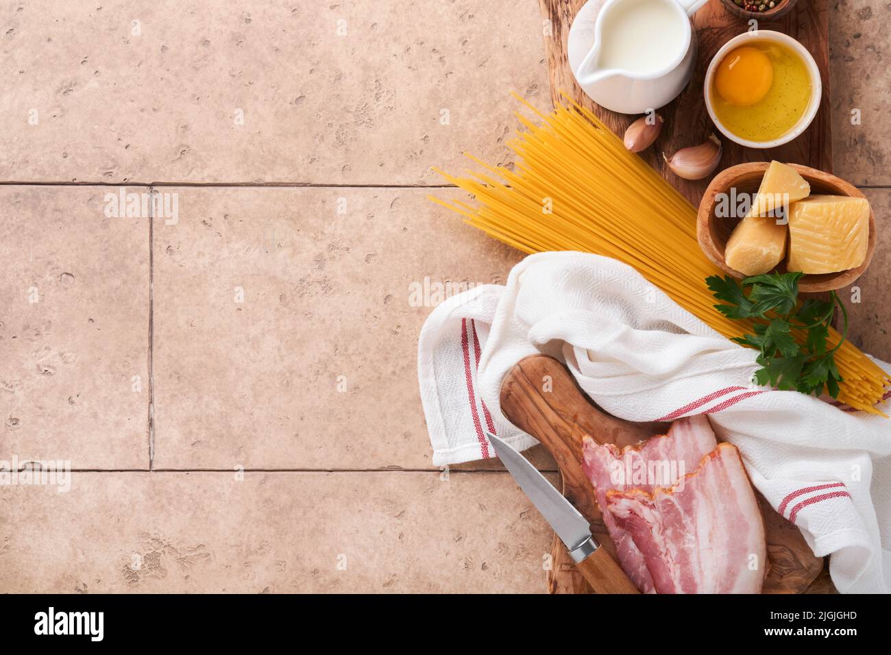 Zutaten für Pasta Carbonara. Traditionelle italienische Pasta Carbonara Zutaten Speck, Spaghetti, Parmesan und Eigelb, Knoblauch. Beigefarbener Tisch mit alten Fliesen Stockfoto