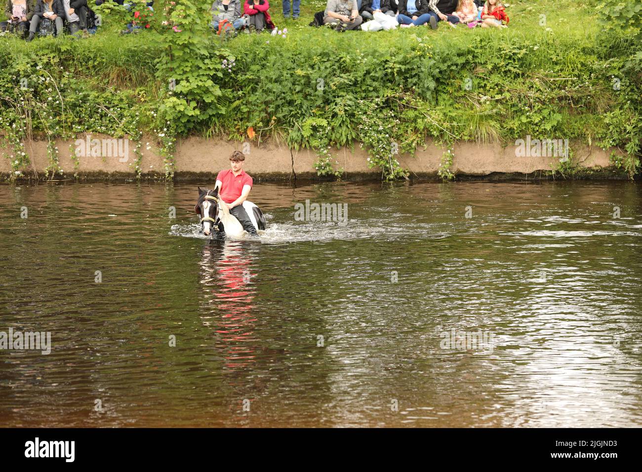 Ein junger erwachsener Mann, der sein Pferd durch den Fluss Eden, Appleby Horse Fair, Appleby in Westmorland, Cumbria reitet Stockfoto