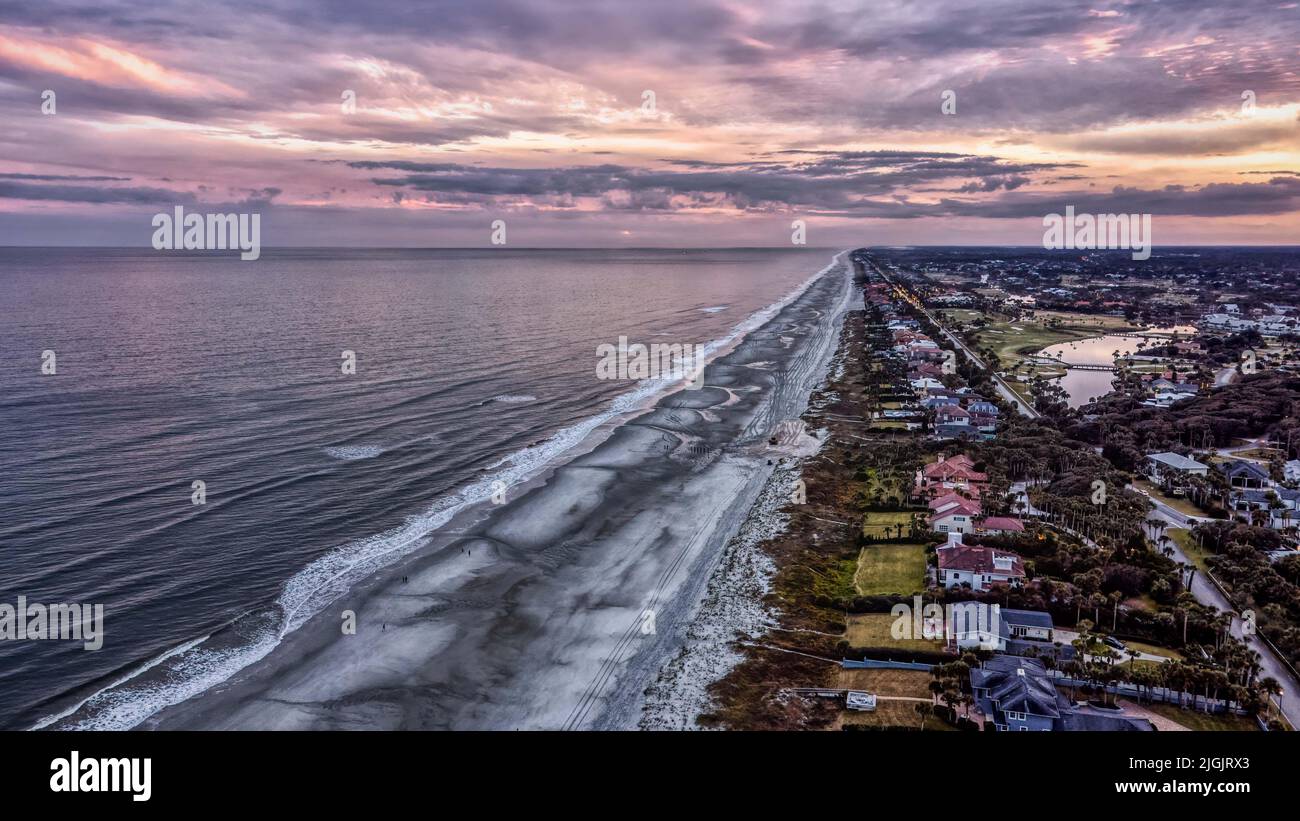 Blick von der Drohne auf Ponte Vedra Beach, FL bei Sonnenuntergang. Weitläufige Küste mit Häusern am Strand, ruhigen Meereswellen und einem farbenfrohen, lebendigen Himmel. Stockfoto
