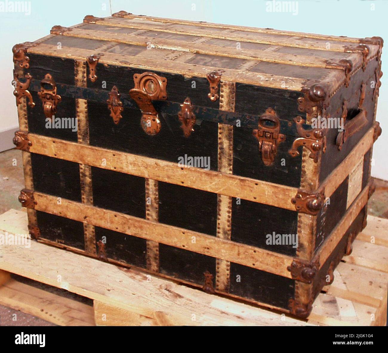 Koffert rechteckiger grüner schwarzer Anzug aus Holz. Lackierte Oberfläche genietet lange und quer Holzstäbe. Messing- und Eisenbeschläge. Ein verstellbarer Griff aus Leder, Messing und Eisen Halterung, auf der kurzen Seite. Ein Handwerk und Halterungen fehlen. Deckel mit vier Eisenscharnieren, Tastensperre, Schnappverschluss, drehbarem Schlüsselschloss. Schlüssel fehlt. Innen in gemusterter Qualität. Holz auf kurzen Seiten für Holzeinlage. Holzeinlage fehlt. Verstauen von Versandnotizen, Aufklebern, auf der kurzen Seite und oben. Weiß bemalter, teilweise unklarer Text '---nie --- N-Telly Theatre New Work' oben. Gehörte dem Frauennachahmer Jo Stockfoto