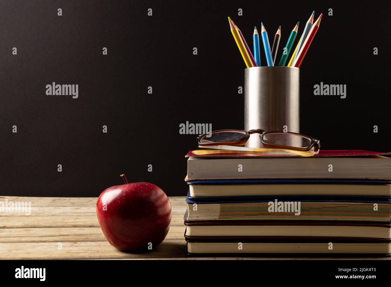 Bild von Stapel von Büchern, Buntstifte in Behälter und Apfel auf schwarzem Hintergrund Stockfoto
