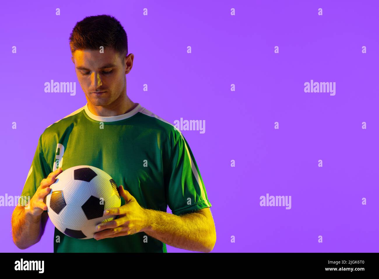 Kaukasischer Fußballspieler mit Fußball über neonpinker Beleuchtung Stockfoto