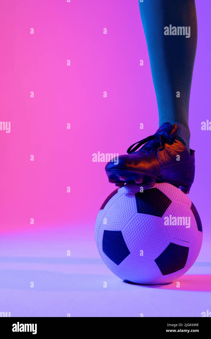 Männlicher Fußballspieler mit Fußball über neonpinker Beleuchtung Stockfoto