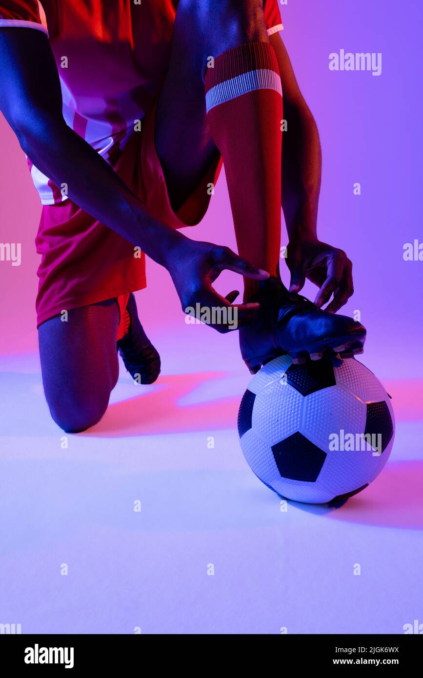 afroamerikanischer Fußballspieler mit Fußballschuhen über neonrosa Beleuchtung Stockfoto