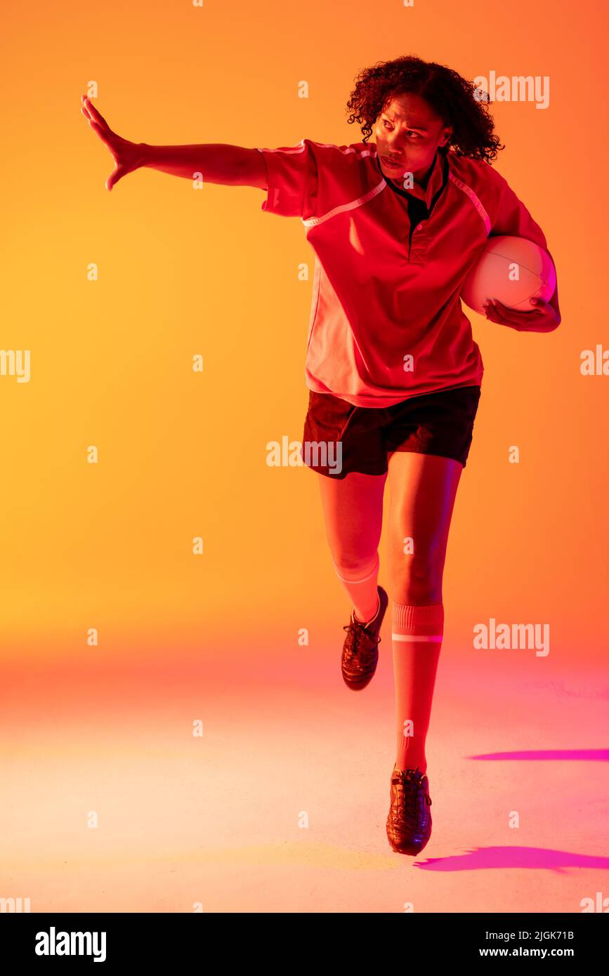 afroamerikanische Rugby-Spielerin mit Armbreit und Rugby-Ball über neonrosa Beleuchtung Stockfoto