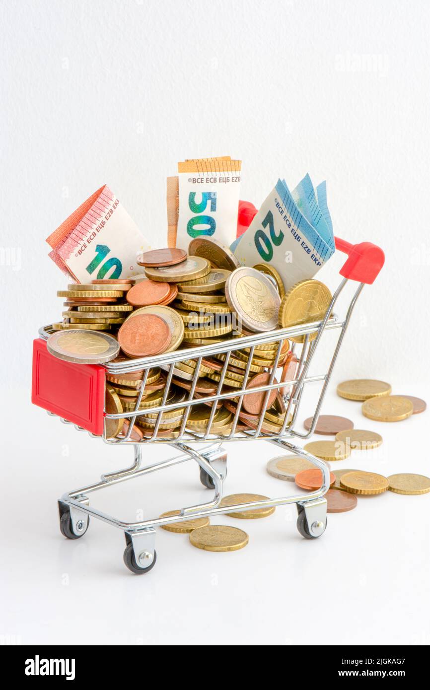 Einkaufswagen überfüllt mit Bargeld (Euro-Münzen und Banknoten). Konzepte von steigenden Preisen, Kaufkraft und steigender Inflation in Europa Stockfoto