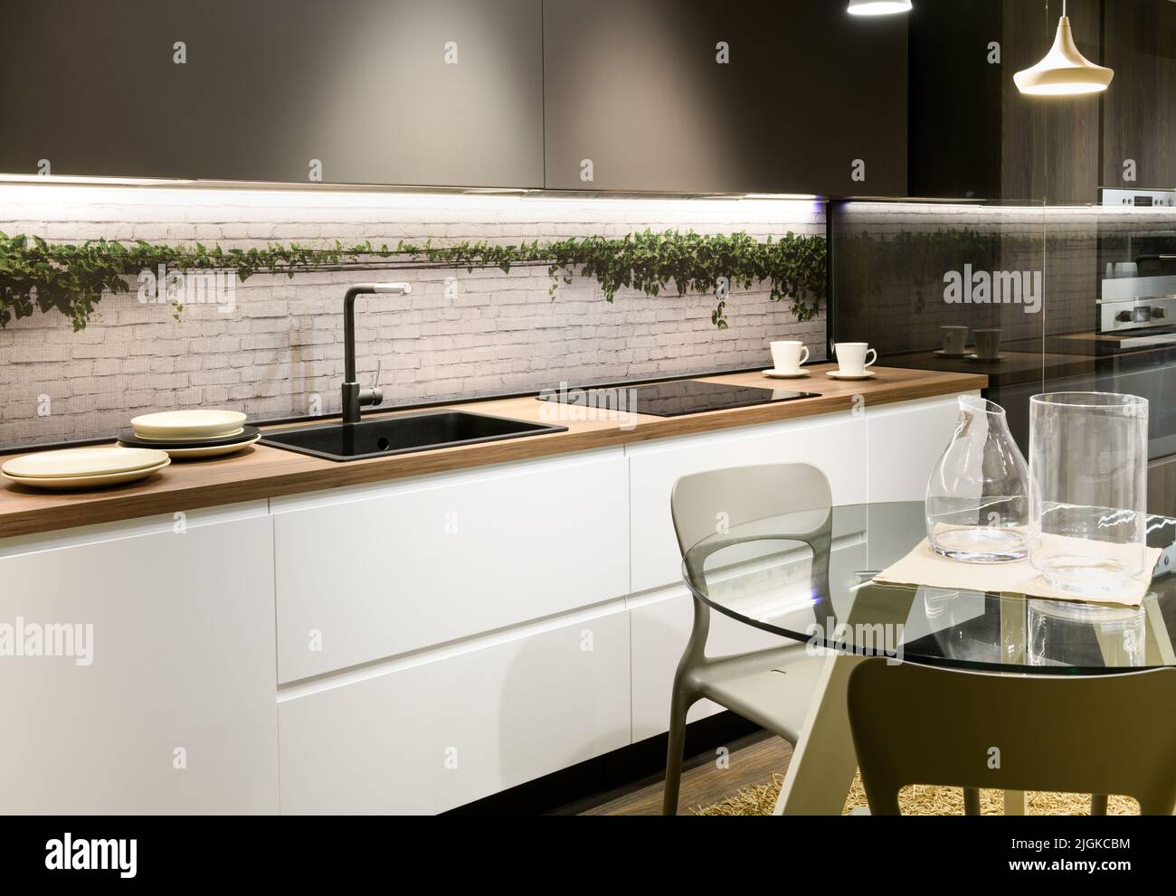 Runder Glastisch mit Gläsern und Stühlen in der Nähe von Theken mit Geschirr und Waschbecken in der modernen Küche zu Hause Stockfoto