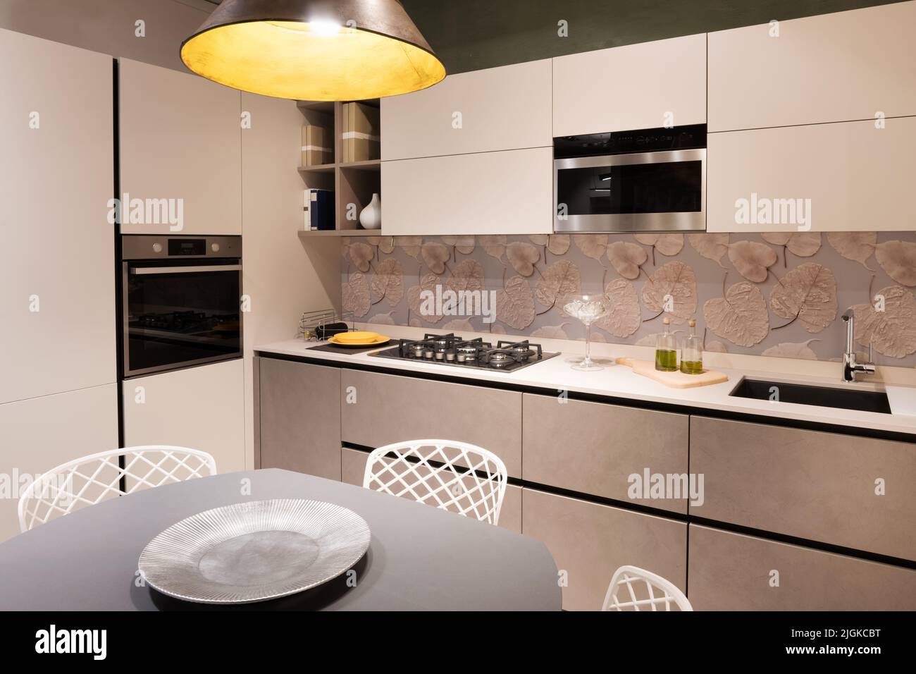 Innenraum der Küche mit modernen Möbeln und eingebauten Geräten mit heller Lampe zu Hause beleuchtet Stockfoto