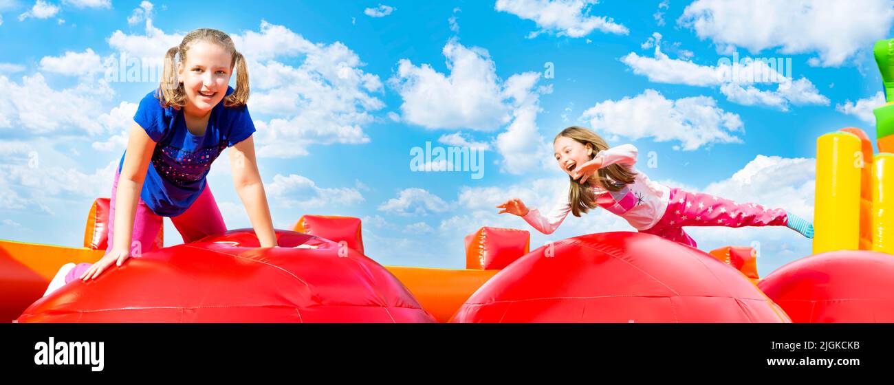 Zwei glückliche kleine Mädchen mit viel Spaß beim Springen von Ball zu Ball auf einem aufgeblasenen Schloss während des Sommers sonnigen Tag. Panorama. Stockfoto