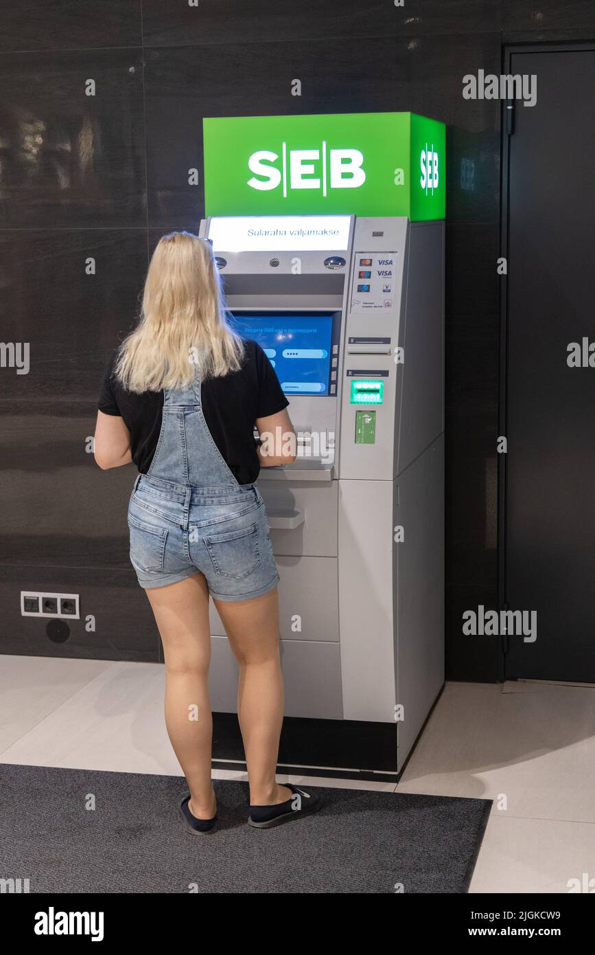 Estnische Bank; eine junge Frau, die Bargeld von einem Geldautomaten oder Geldautomaten der SEB Pank, einer estnischen Bank, Tartu, Estland, Europa, erhält Stockfoto