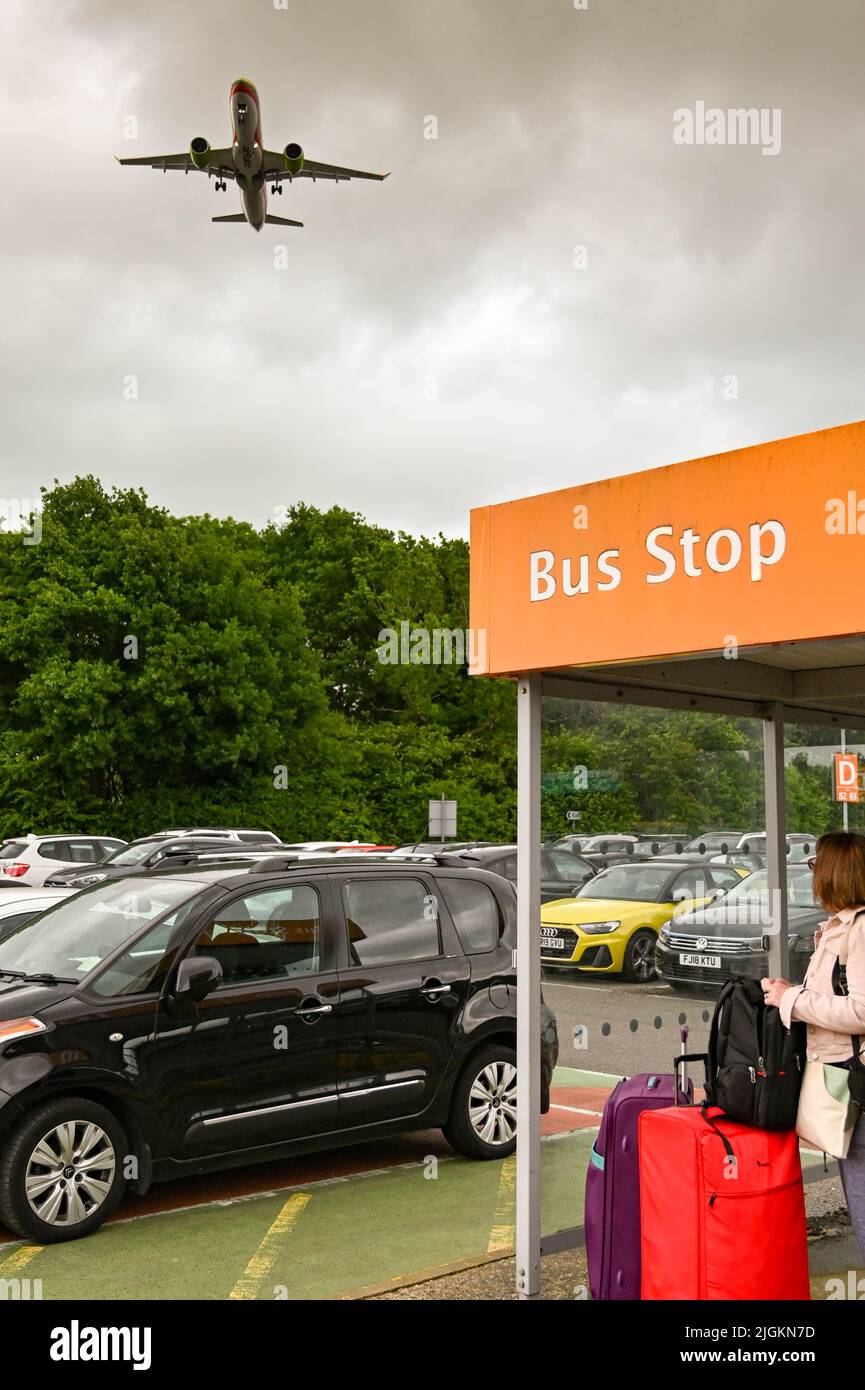 London, England - 2022. Juni: Person, die an einer Bushaltestelle auf einem der Langzeitparkplätze am Flughafen London Gatwick wartet. Ein Flugzeug fliegt über uns. Stockfoto