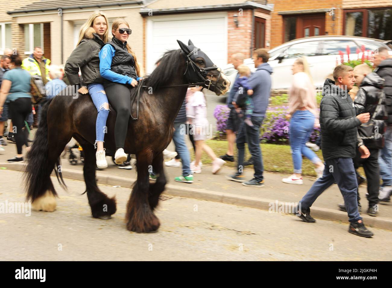 Zwei Mädchen im Teenageralter reiten auf einer schwarzen Zigeunercob entlang der Straße in Appleby, Appleby Horse Fair, Appleby in Westmorland, Cumbria Stockfoto