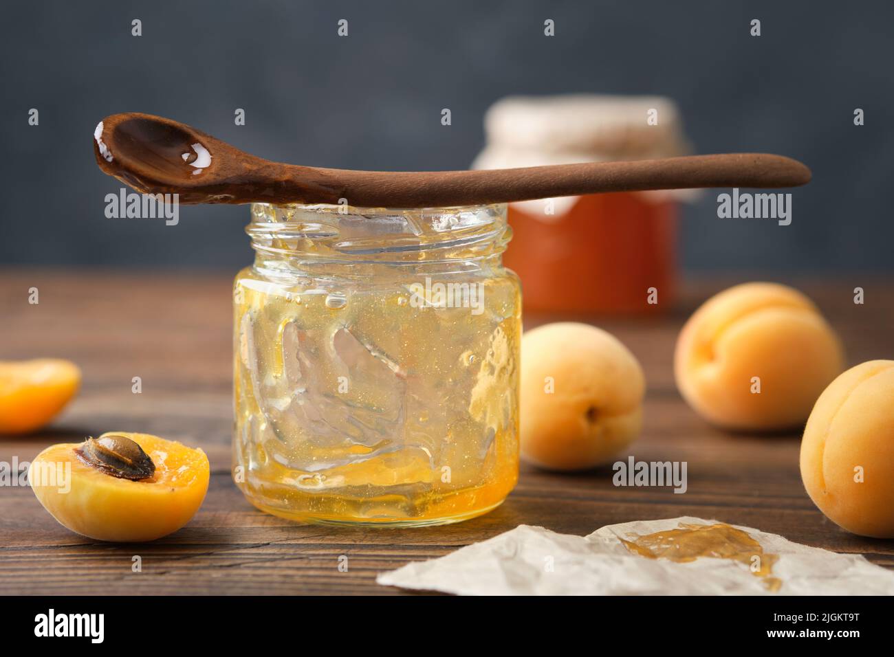 Leeres Glas mit verzehrter Aprikosenmarmelade. Leeres Glas mit hausgemachter Aprikosenmarmelade, Löffel und reifen Aprikosenfrüchten auf dem Küchentisch. Stockfoto