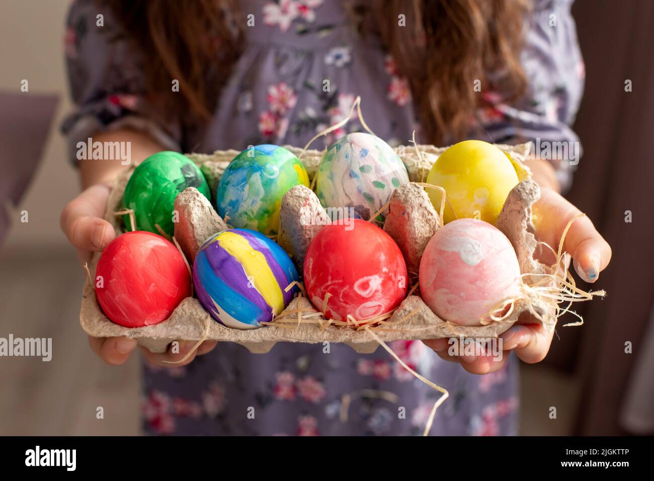 Hände eines Mädchens in einem Kleid, das ein Papptablett mit bunten handbemalten Eiern hält Stockfoto